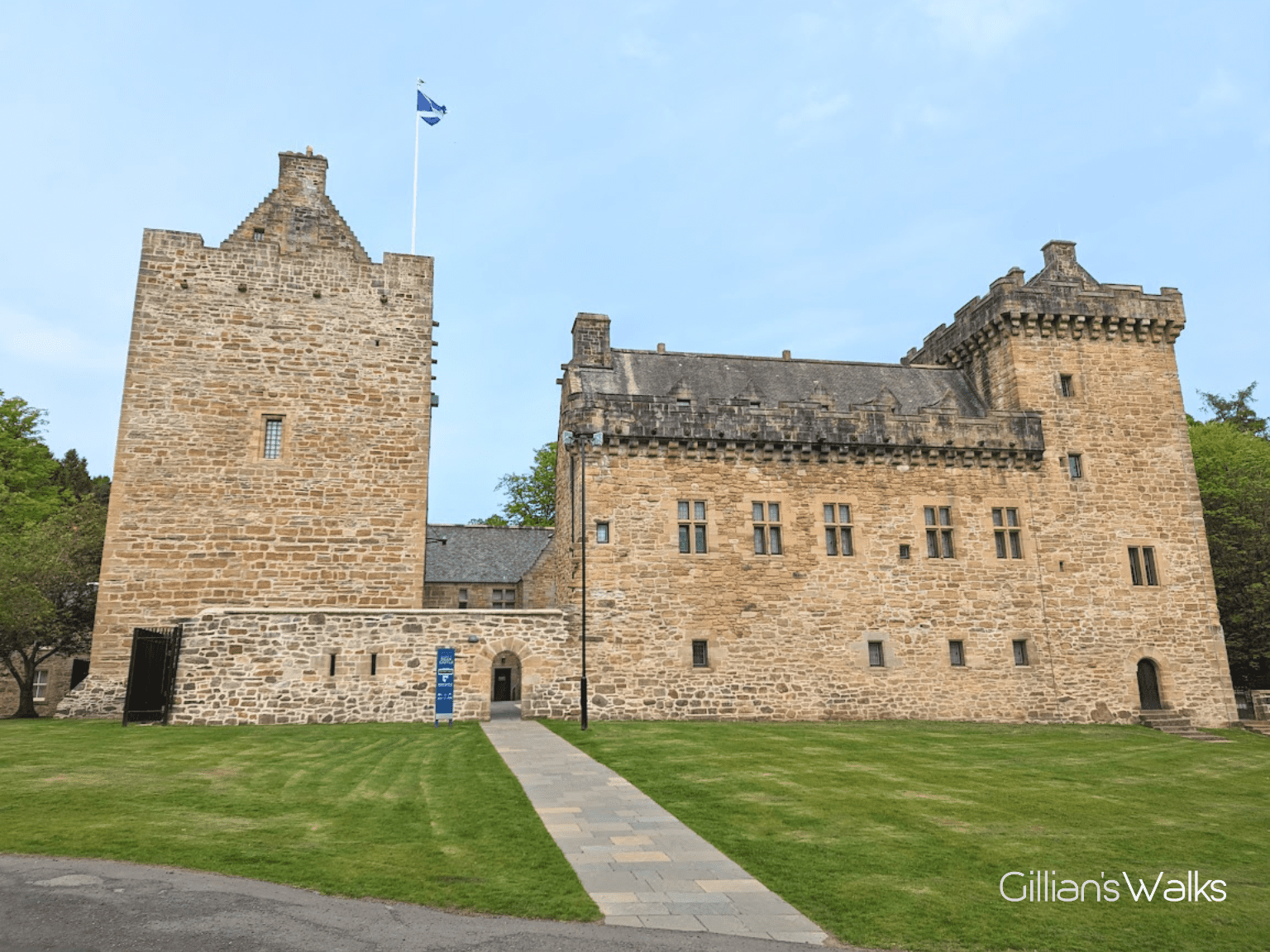 Medieval castle built with yellow sandstone blocks. There is a slabbed path leading towards it and a well-maintained grassy area either side of the path.