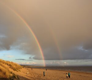 A double rainbow touches a sandy beach in front of dark grey clouds