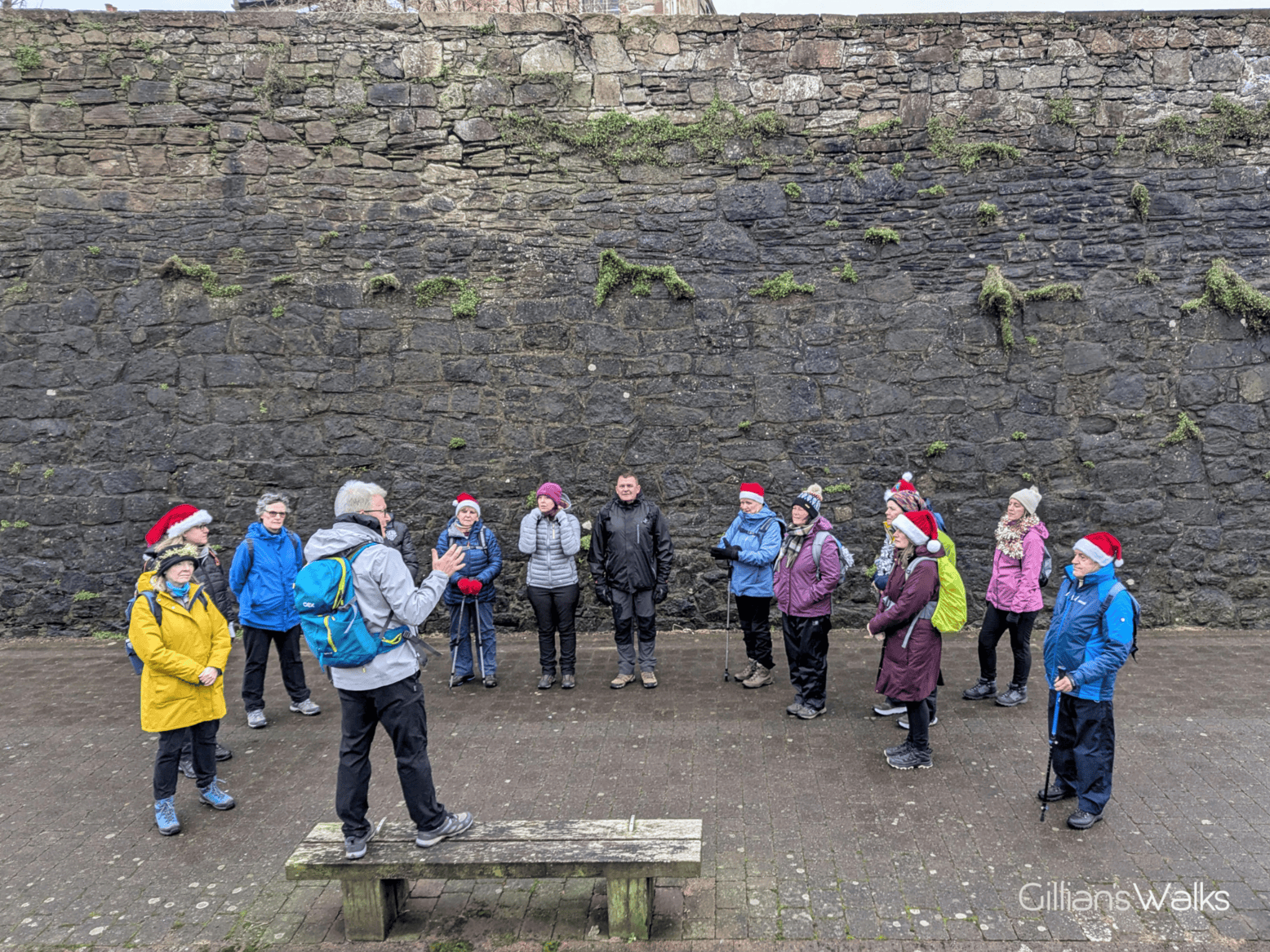 Group of 12 walkers standing in a semi circle around a man giving a talk. The huge walls of Cromwell's Citadel tower above them, giving a real sense of scale.