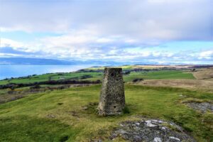 Trig point overlooking grassy farmland and the Firth of Clyde