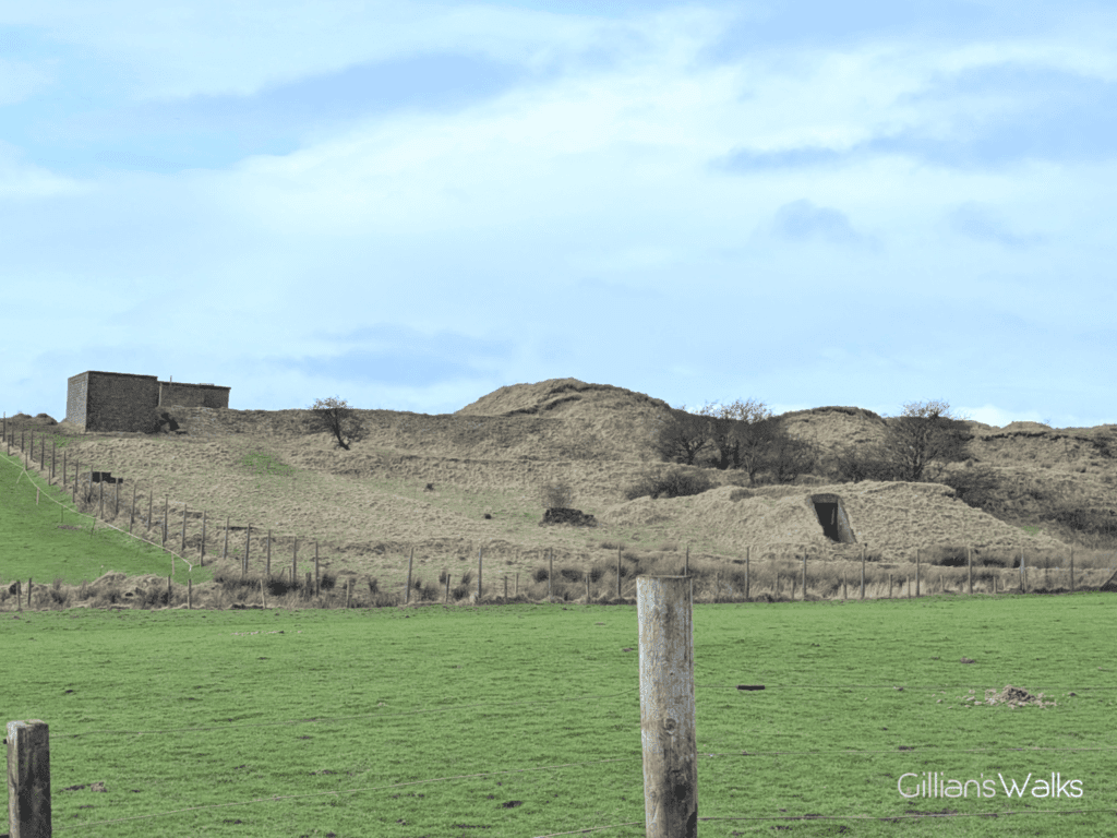 Earthworks at Montfode seen from across a grassy field. There is a rectangular tunnel entrance and some brick buildings.