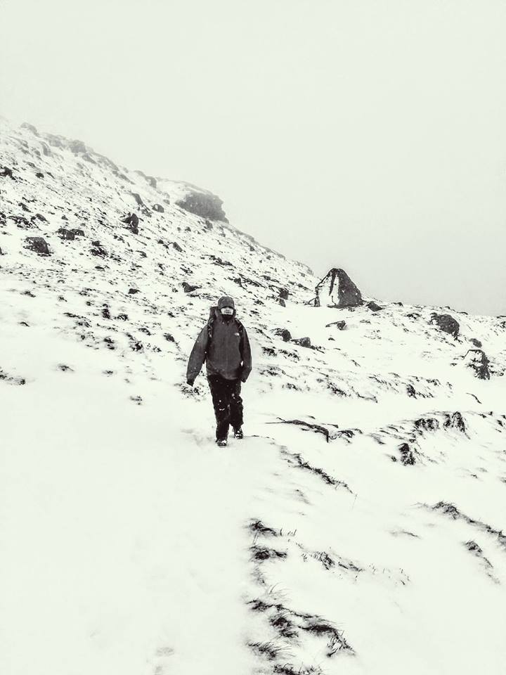My friend walking towards me on a snow-covered rocky hillside, with very poor visibility all around. 