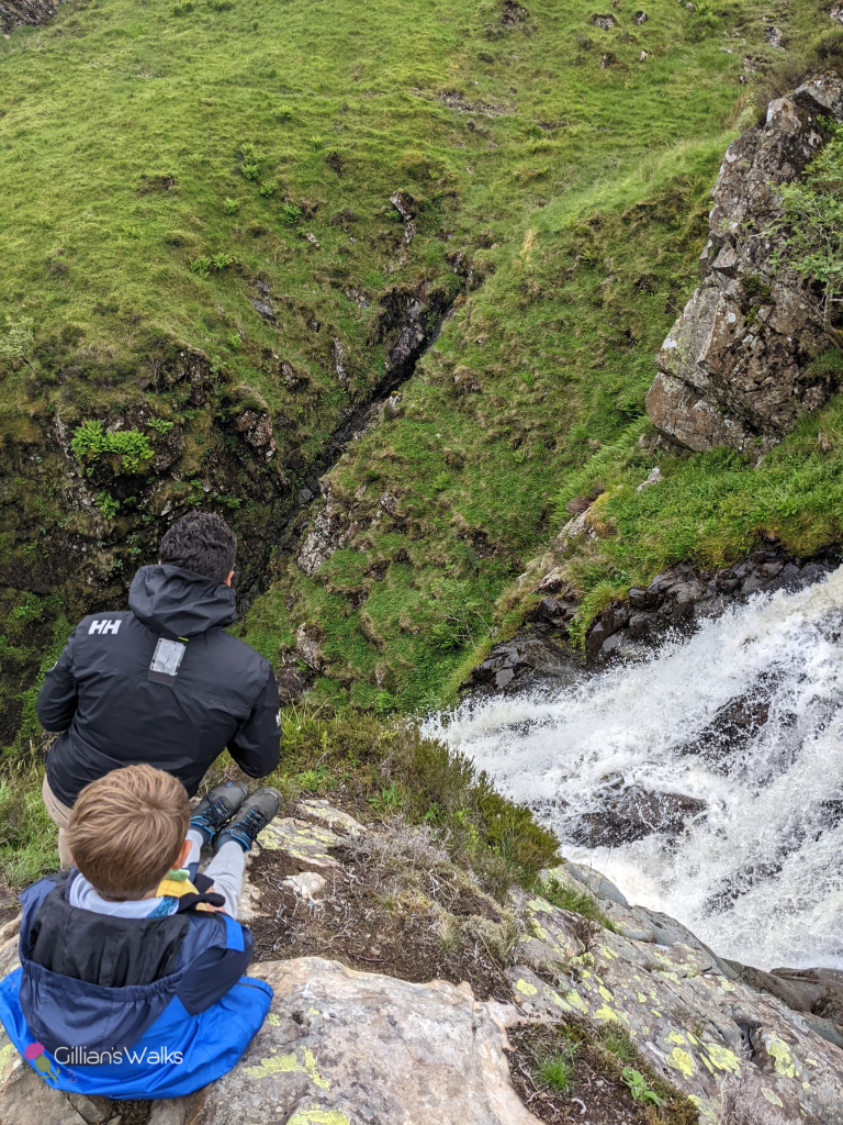 My husband and 9 year old son crouching on top of a rock above a cascading waterfall 