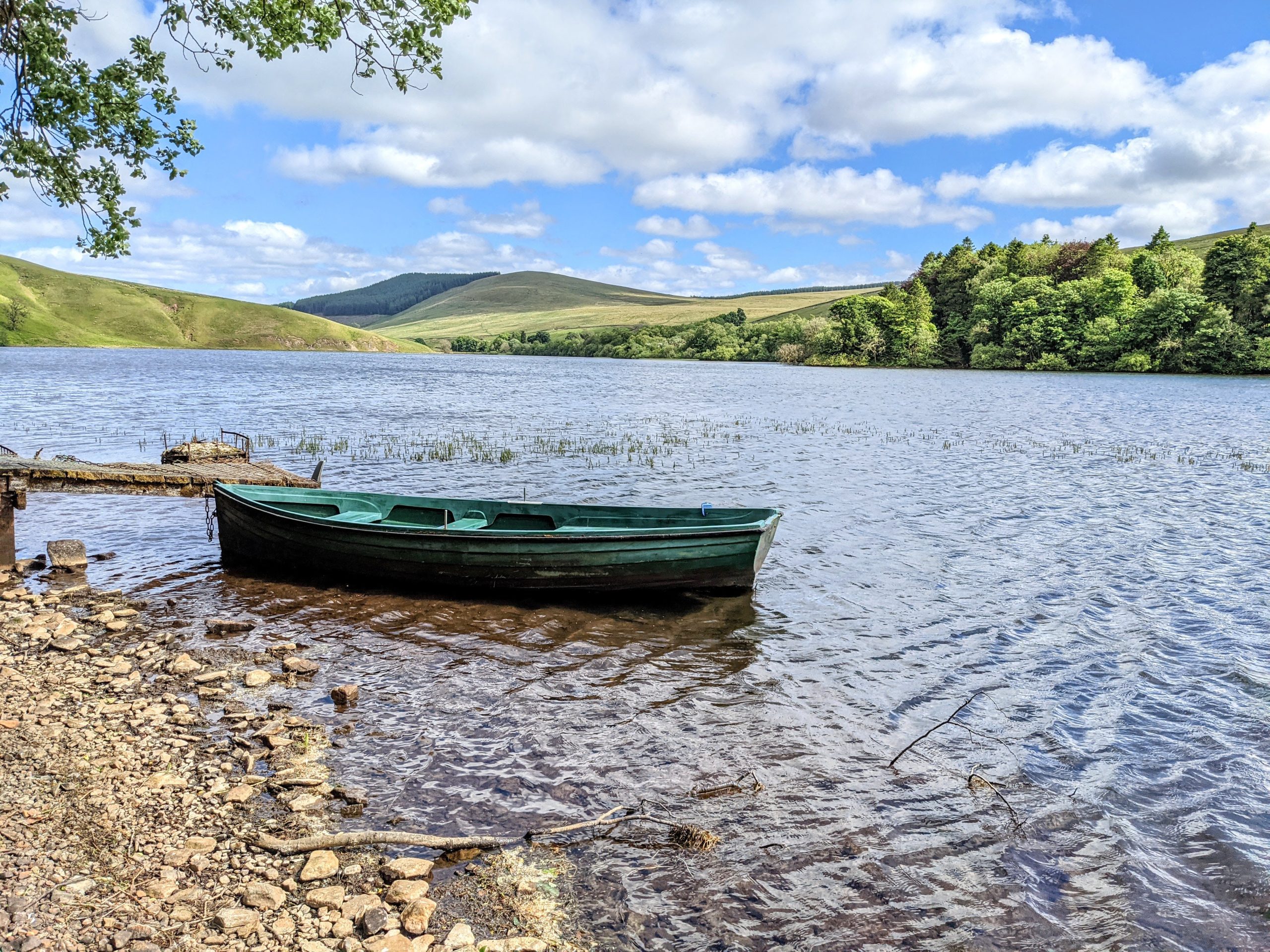 Glenbuck Loch with a small wooden rowing boat in the foreground and hills and countryside surrounding