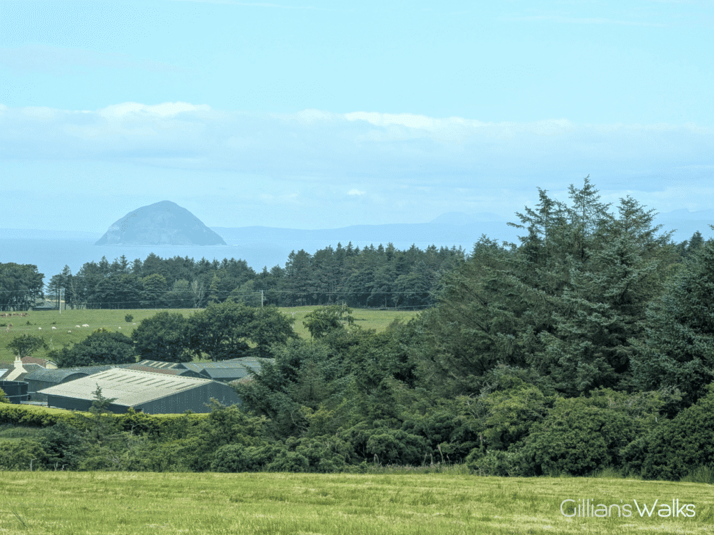 A view to Ailsa Craig standing tall beyond lush green farmland