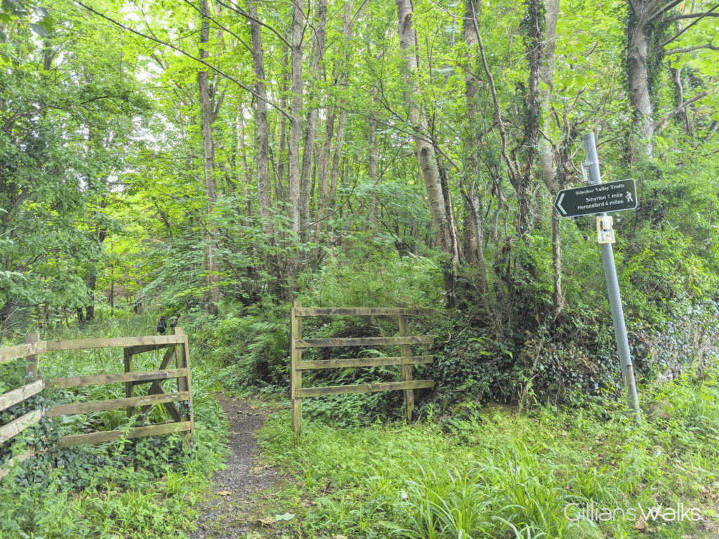 An inviting wooden gateway leading into the woods, with signage indicating there is a walk inside