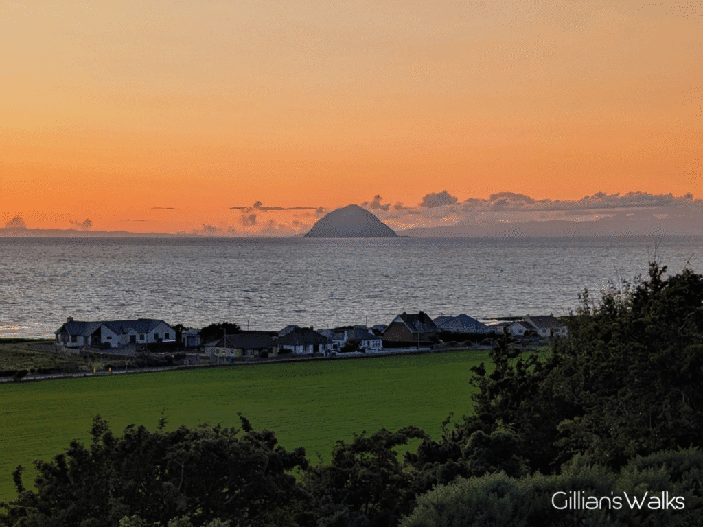 Orange glow of the sun setting against a silhouette of Ailsa Craig seen across the Clyde.