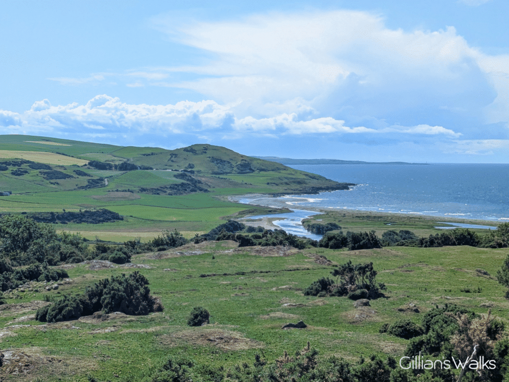 View down from a hilltop over grassy farmland and in the distance the sea, the mouth of the river Sinchar and the headland at Downan Hill.