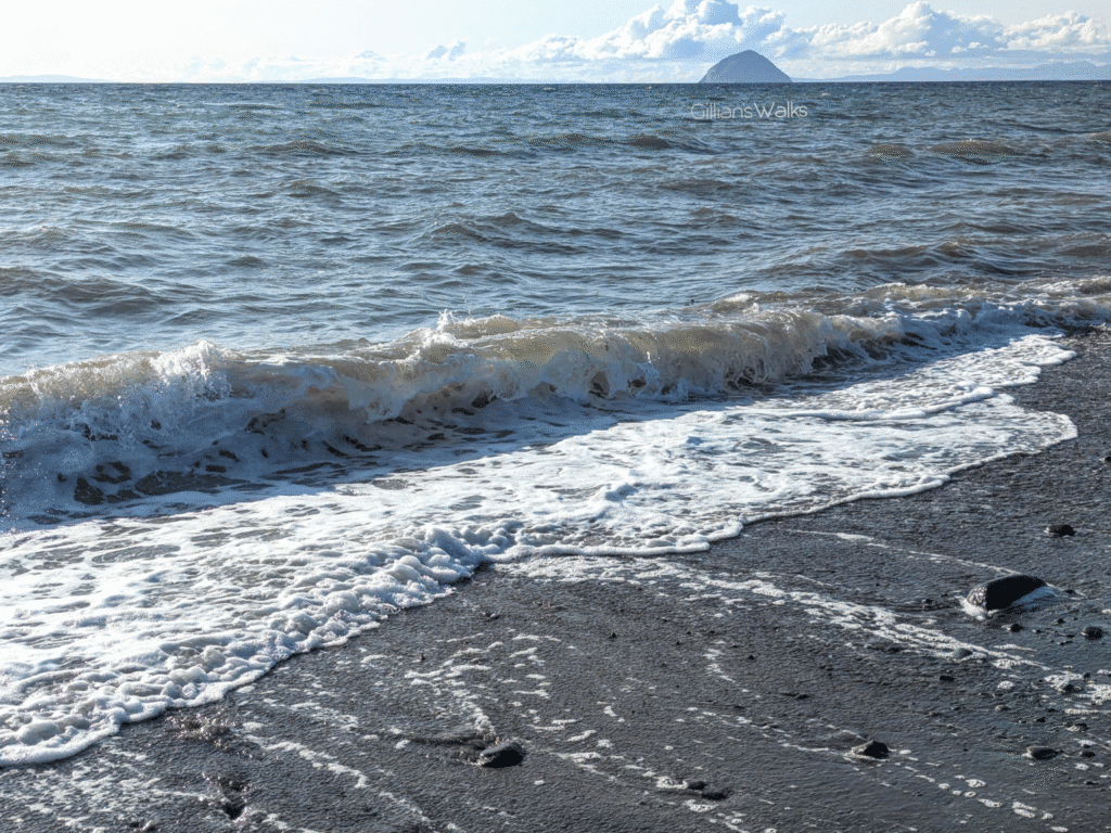 Gentle wave breaking on the shore at Ballantrae with Ailsa Craig visible on the horizon