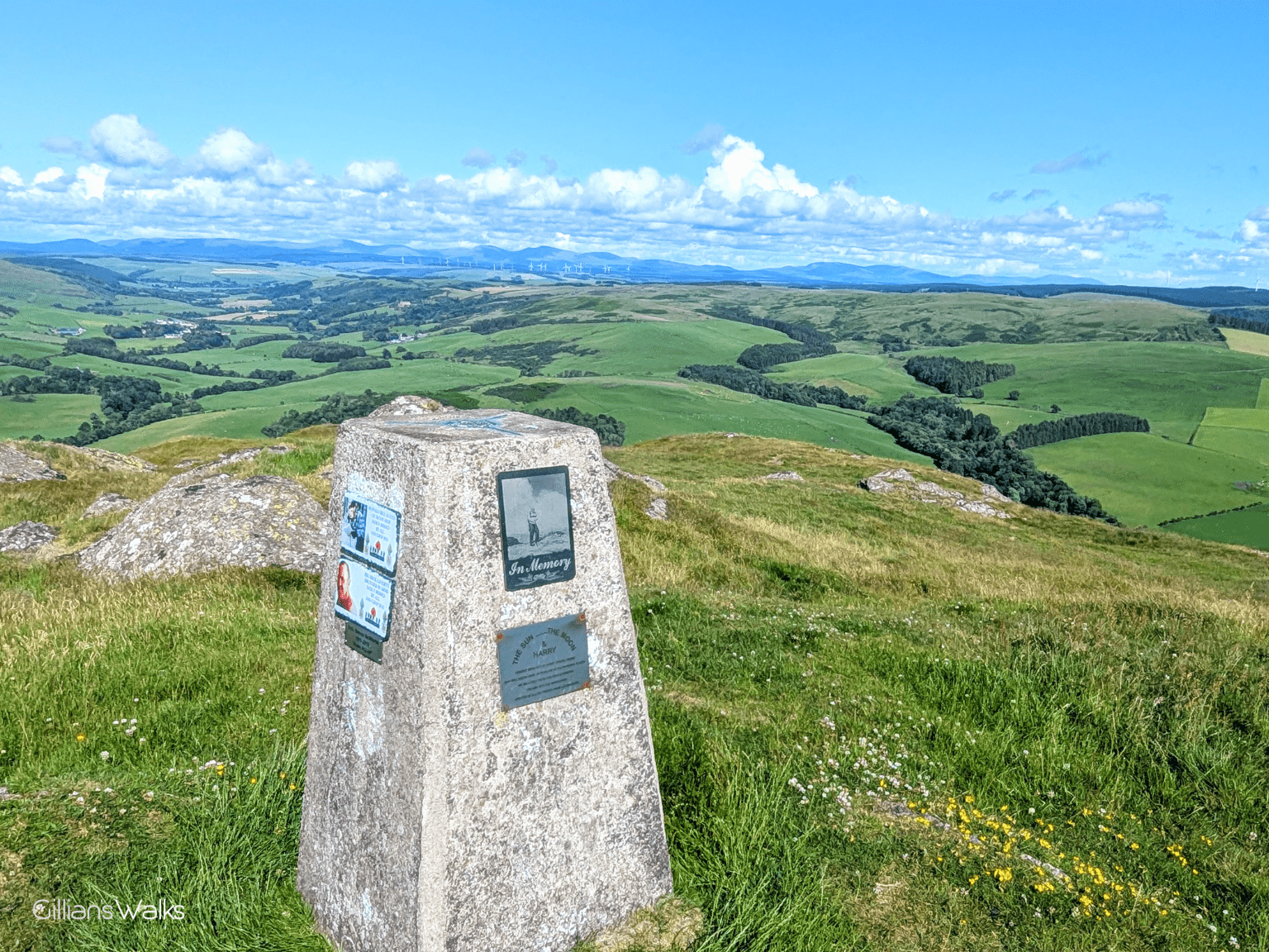 Stone trig point at the top of Knockdolian Hill, with memorial plaques attached to the two visible sides