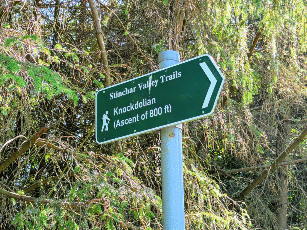Green metal Stinchar Valley Trails sign pointing to the right for 'Knockdolian' 