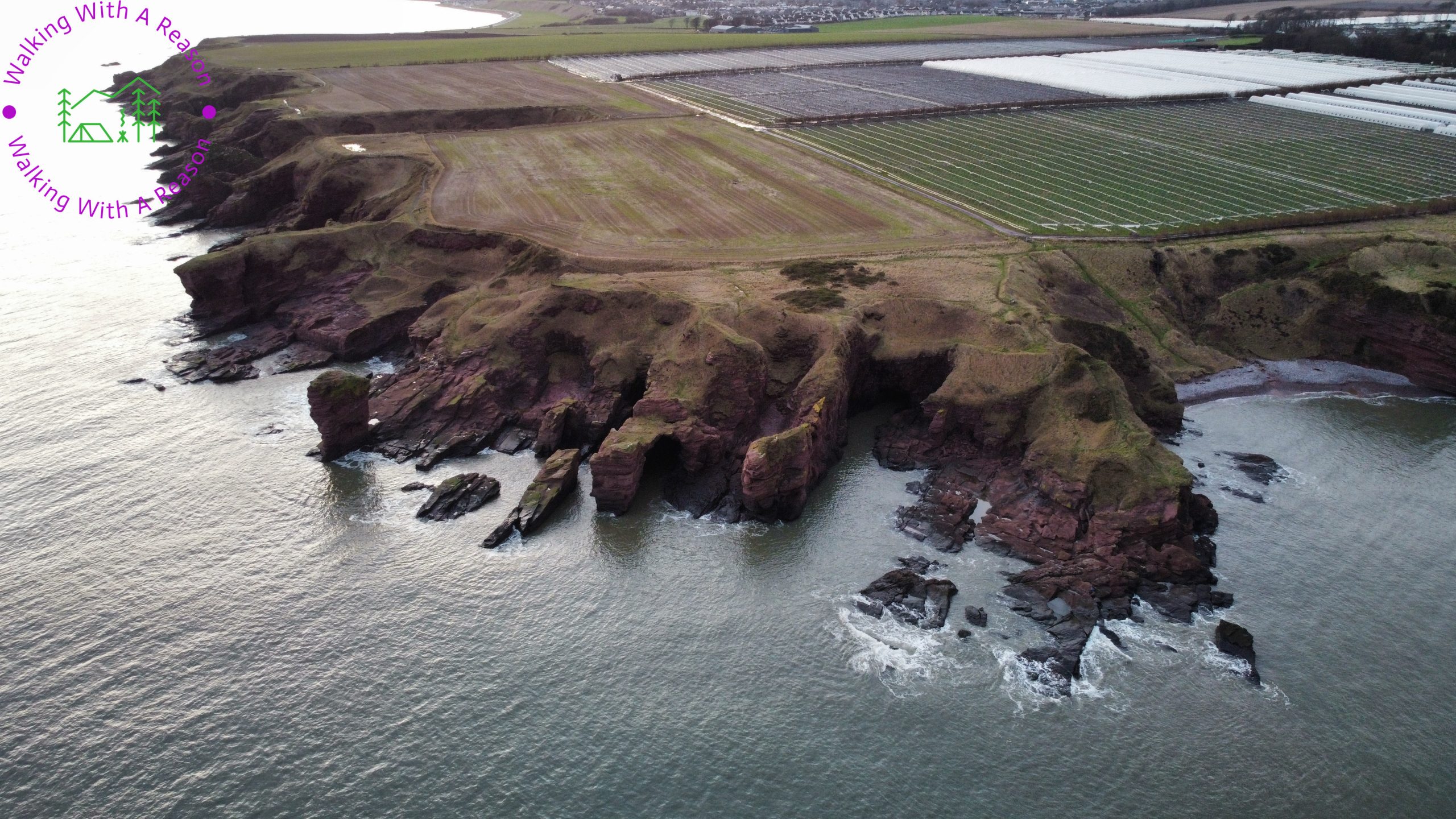 A drone image looking down at the cliffs from the sea, the angle showing the flat farmland giving way to a dramatic rugged coastline
