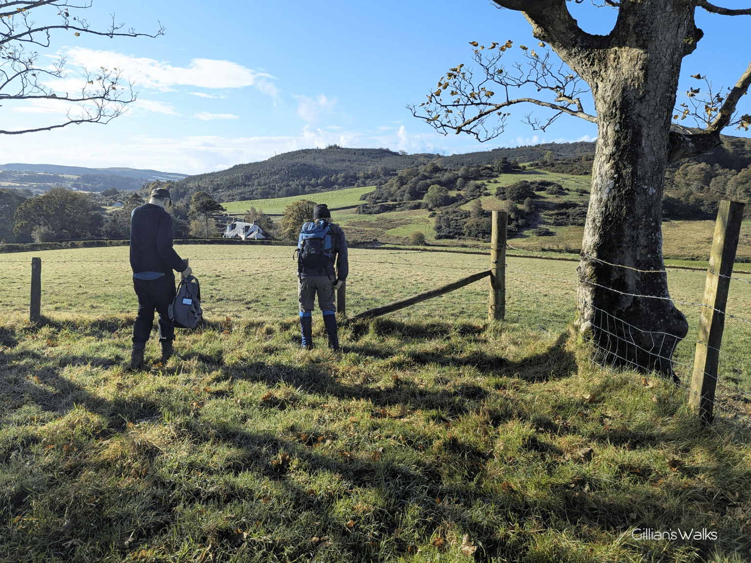 Two walkers preparing to squeeze through fence wire into a neighbouring field