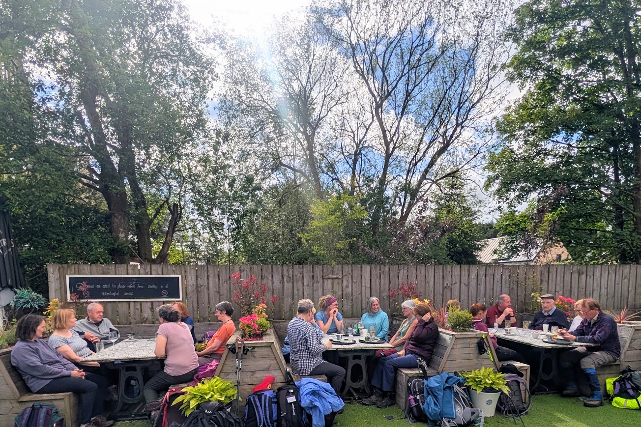 Our large group taking over three tables in Carriages pub beer garden, which has wooden bench style seating and lots of flowers.