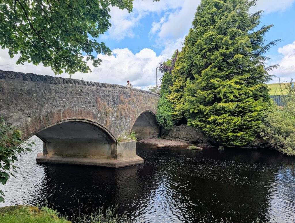 A twin arch stone bridge over the Gryffe Water with one man standing on top