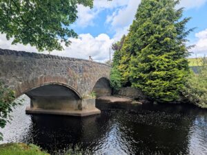 A twin arch stone bridge over the Gryffe Water with one man standing on top