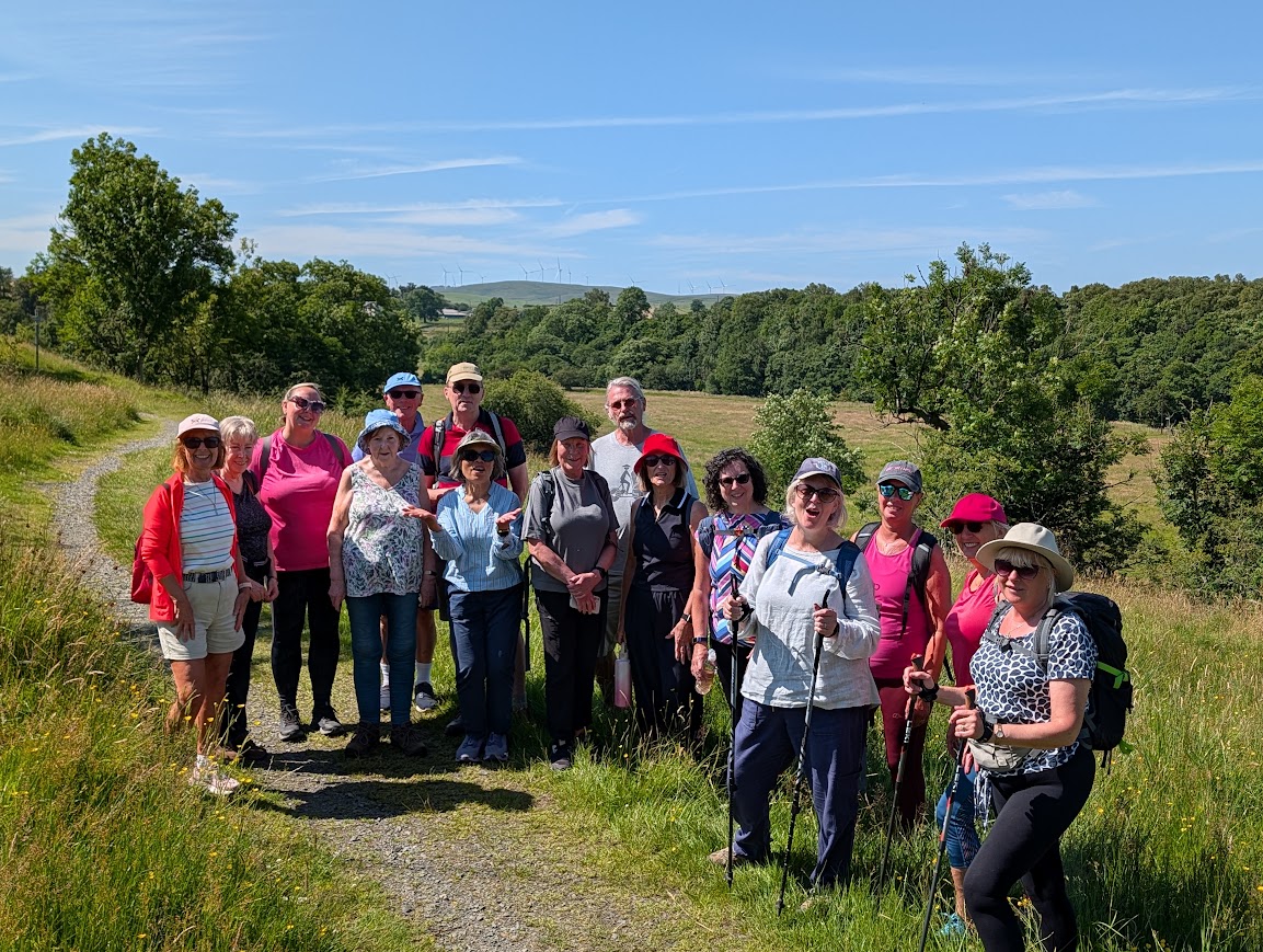 Large group of walkers posing for a photo on higher ground, surrounded by trees and peaceful countryside