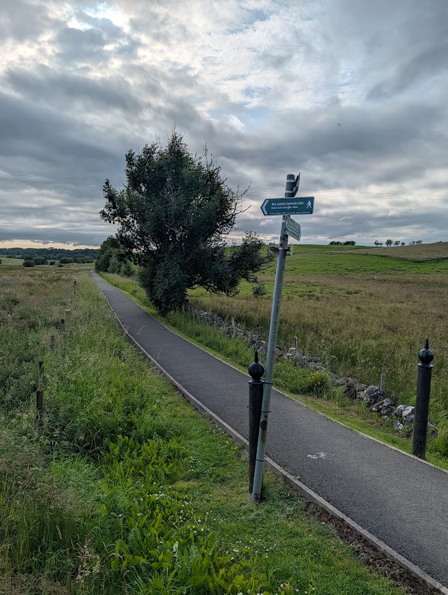 Long, straight, narrow paved walkway with a metal signpost pointing along it.