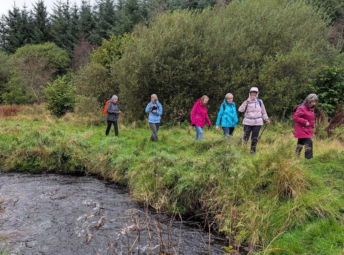 Group of ladies in waterproofs, walking along the edge of the Dippol Bun which is in spate