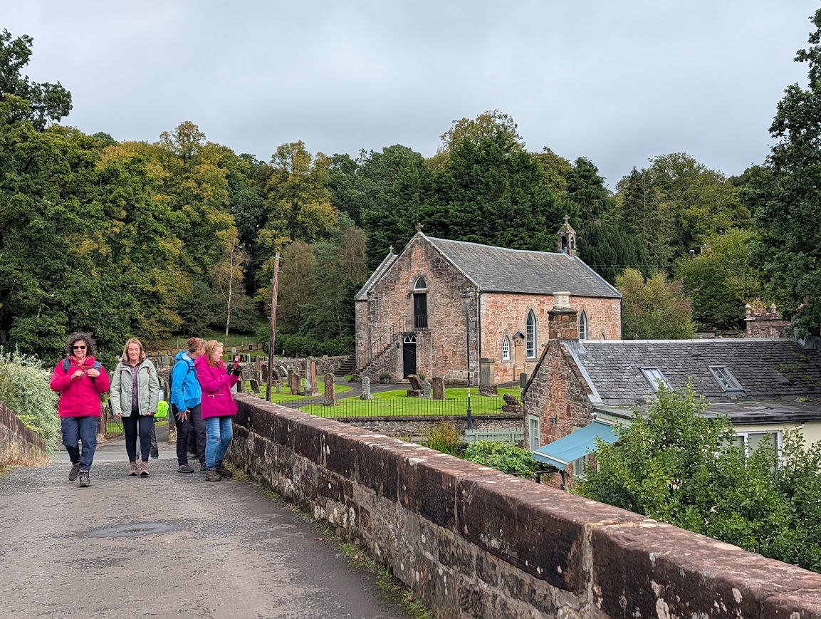 Several ladies on the old stone bridge in Sorn, with the old Parish Church in the background