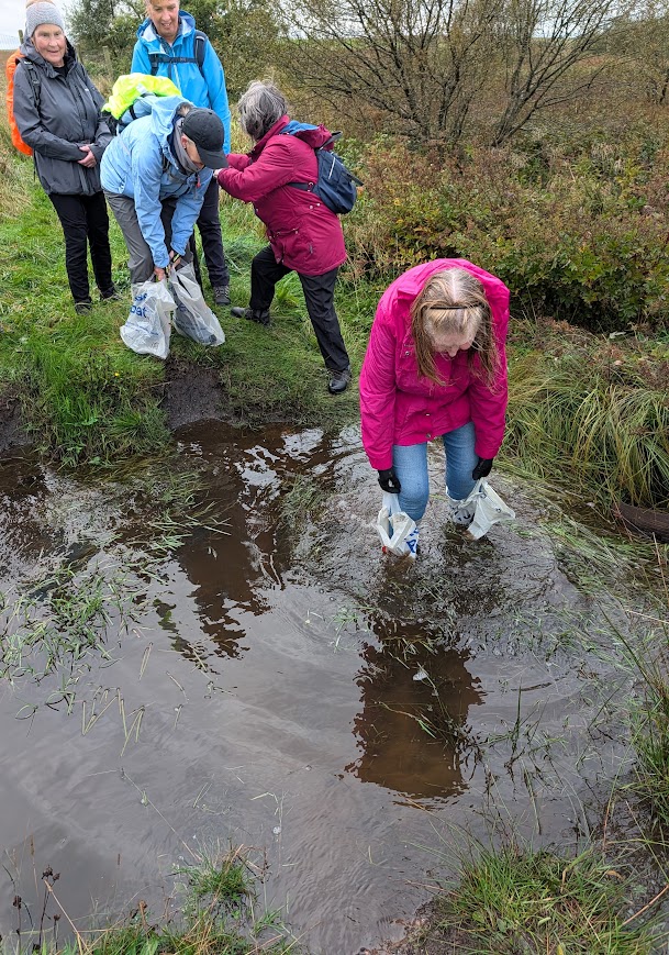 A lady walks through water up as high as her shins wearing a plastic shopping bag on each foot to avoid getting wet.